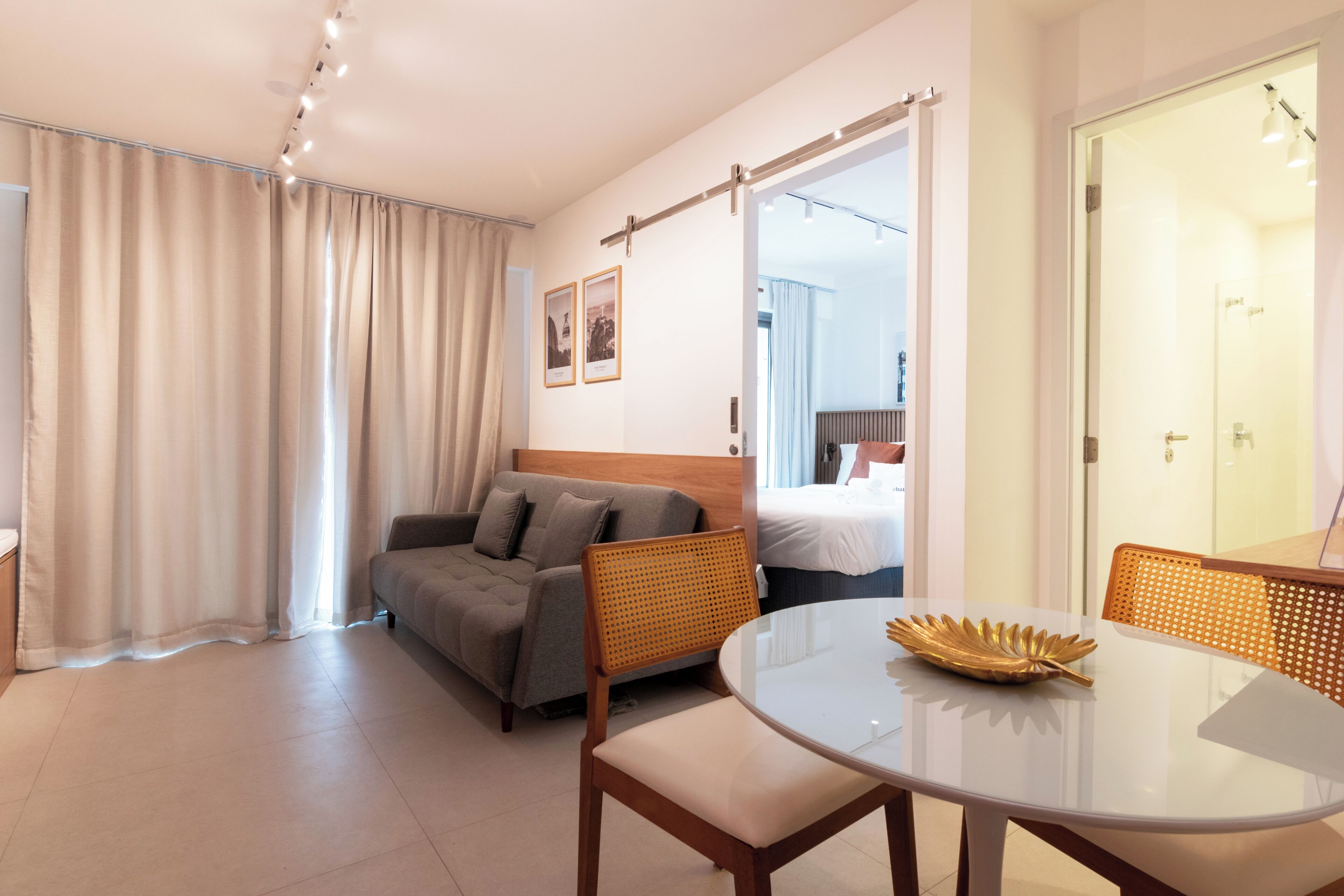 A modern hotel room with a sofa, a round dining table, and a bed with a view.