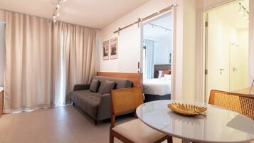 A modern hotel room with a sofa, a round dining table, and a bed with a view.