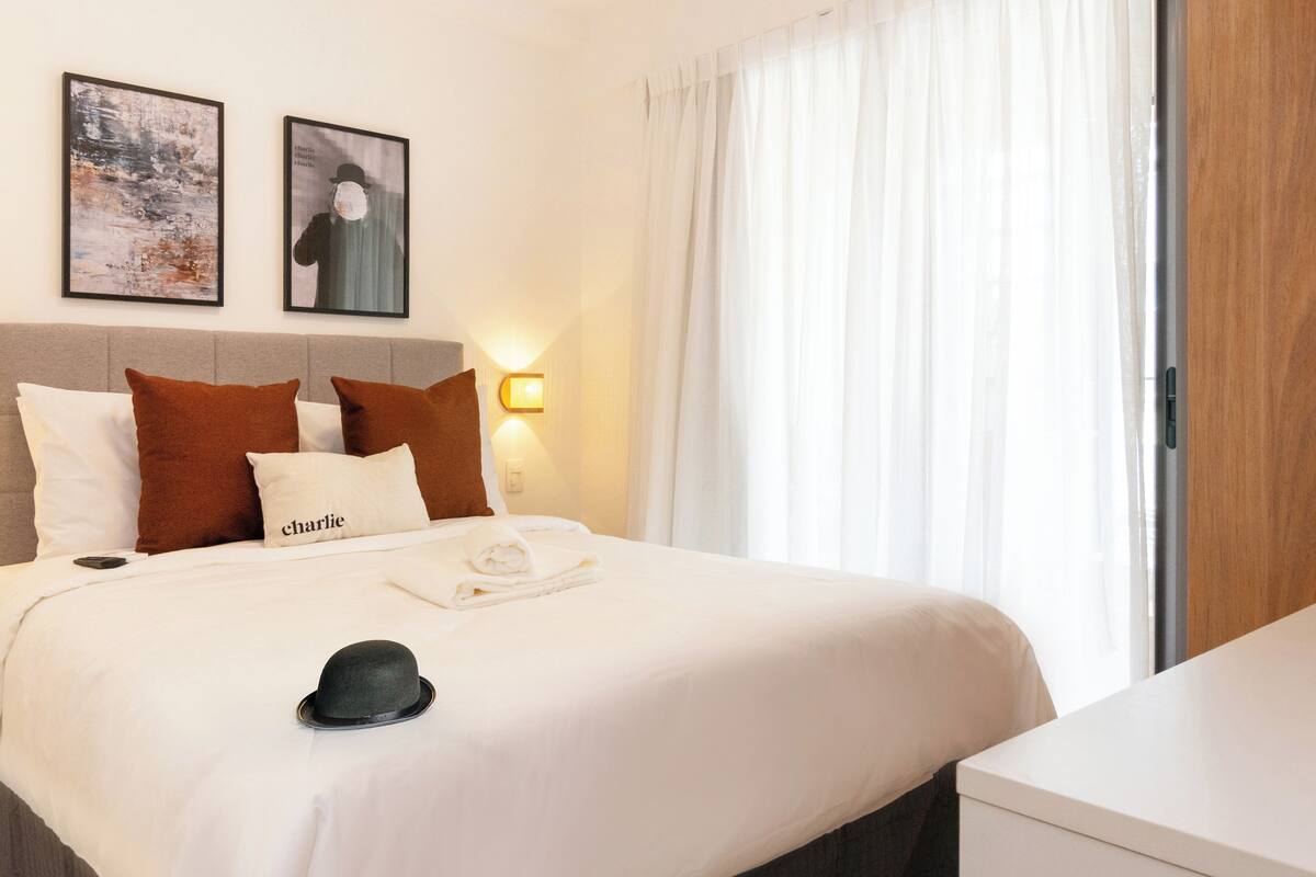 A hotel room with a neatly made bed, a bedside lamp, and two framed pictures on the wall.