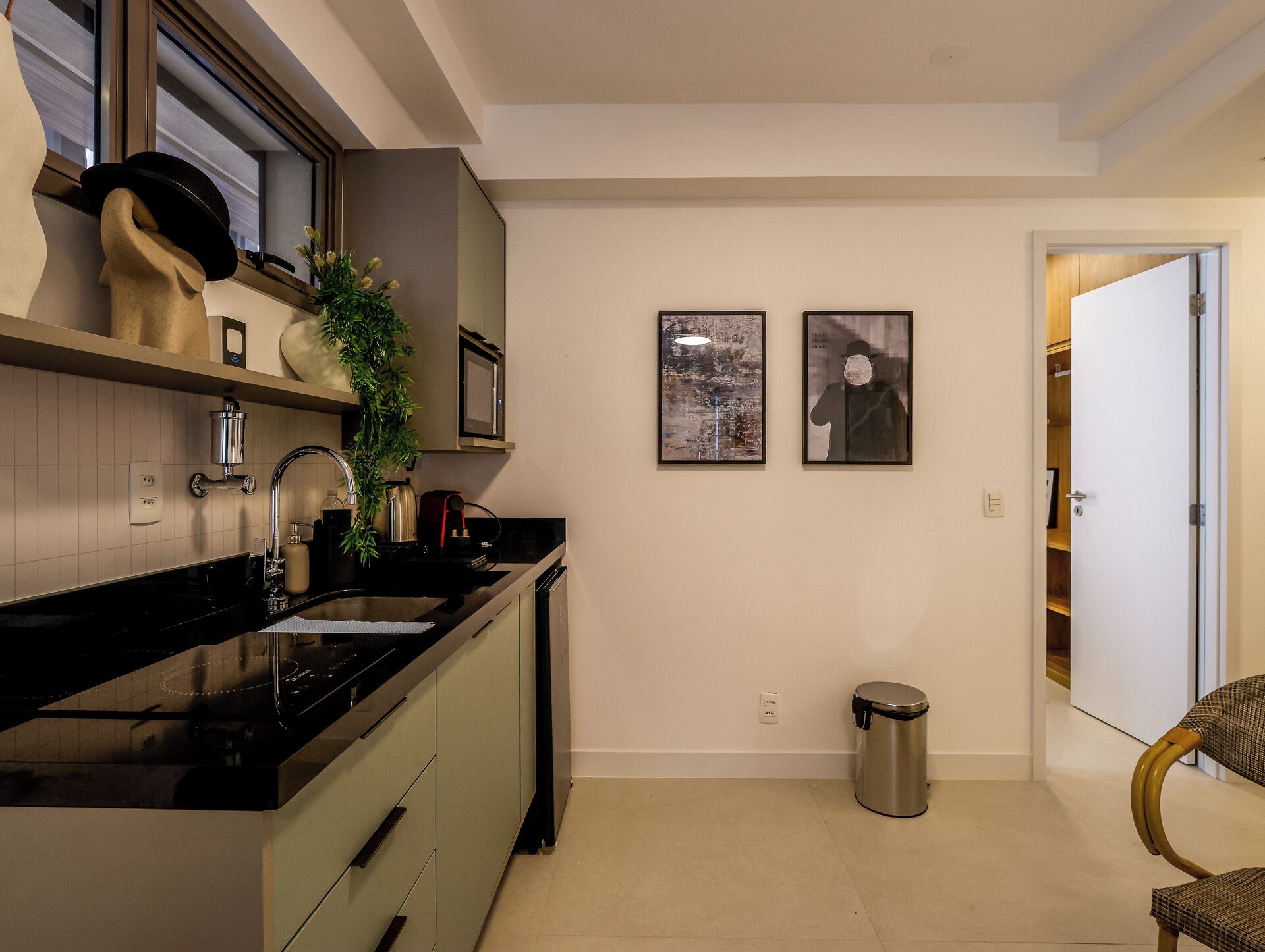 A modern kitchen with a black countertop, stainless steel sink, and a trash can. There are two framed pictures on the wall and a door leading to another room.