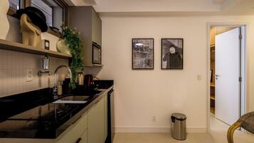A modern kitchen with a black countertop, stainless steel sink, and a trash can. There are two framed pictures on the wall and a door leading to another room.