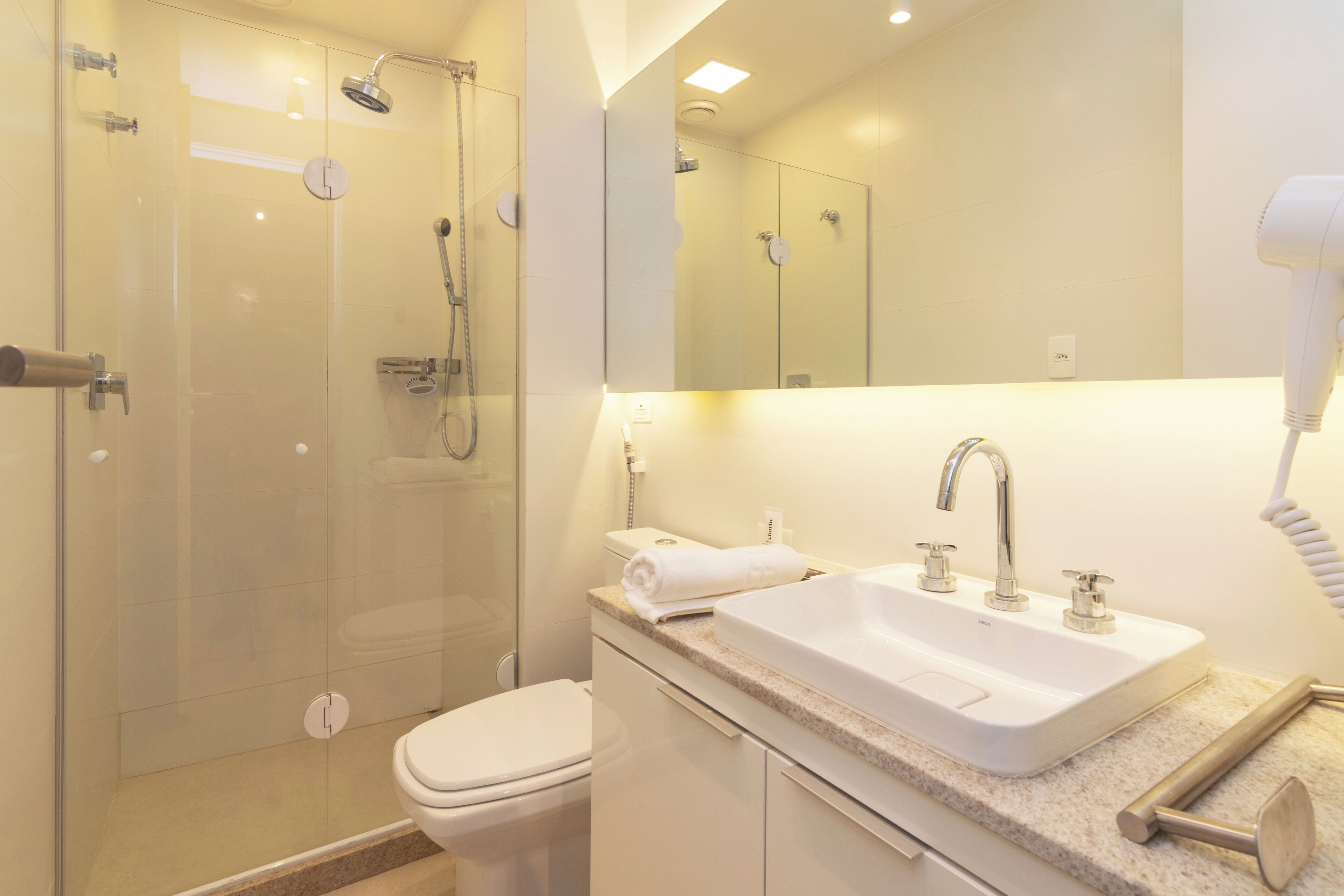 Une salle de bain moderne avec une douche à parois de verre, un lavabo blanc et un sèche-cheveux.