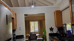 A modern kitchen with wooden cabinets, a stainless steel refrigerator, a dining table with chairs, and a large window with curtains. - Tropical Tranquility in Jamaica (Richmond Estate)