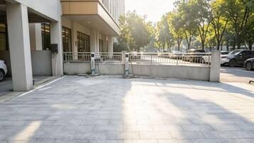 A paved outdoor area with a building entrance, a gated parking area, and a row of parked cars.