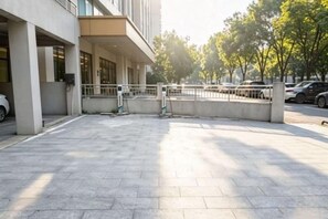 A paved outdoor area with a building entrance, a gated parking area, and a row of parked cars. - Vienna International Hotel (Zhuzhou Railway Station Central Square Branch) (Zhuzhou)