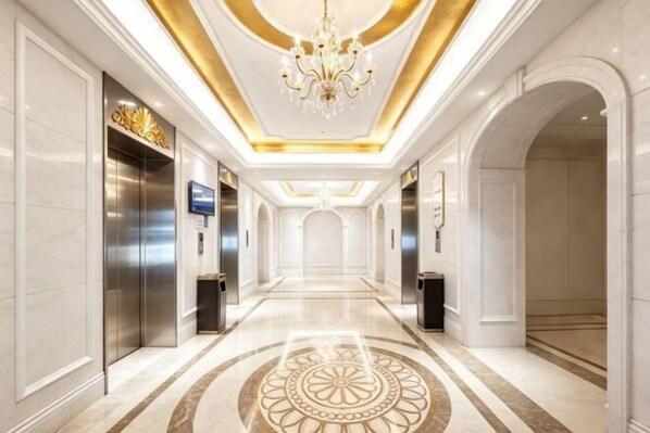 A hotel corridor with a chandelier, elevators, and a patterned floor.