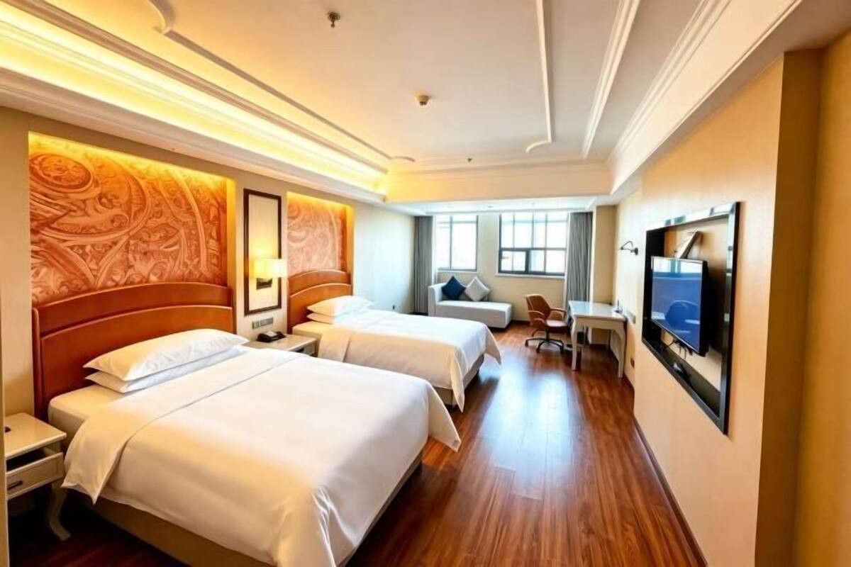 A hotel room with two beds, a TV, a desk, and a window.