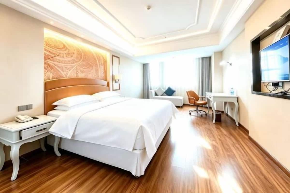 A hotel room with a large bed, a desk, a chair, a TV, and a window.