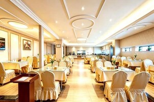 Un comedor de hotel con varias mesas y sillas, un bufé central y una cocina al fondo.