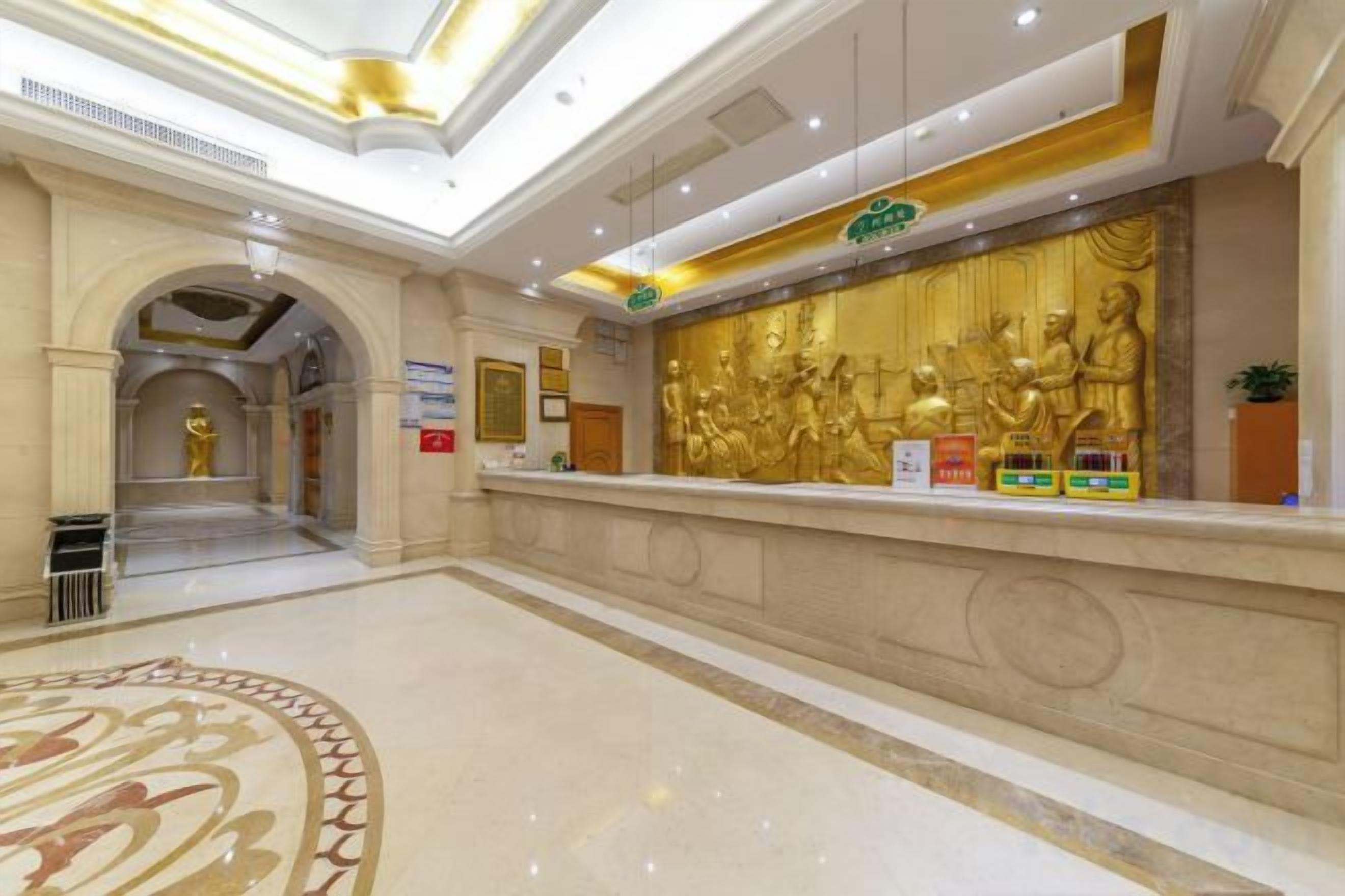 A hotel reception area with a marble floor, a reception desk, and a large golden statue.