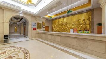 A hotel reception area with a marble floor, a reception desk, and a large golden statue.
