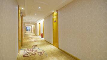 A hotel corridor with carpeted floors, doors on both sides, and a patterned wall.
