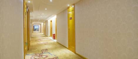A hotel corridor with carpeted floors, doors on both sides, and a patterned wall.