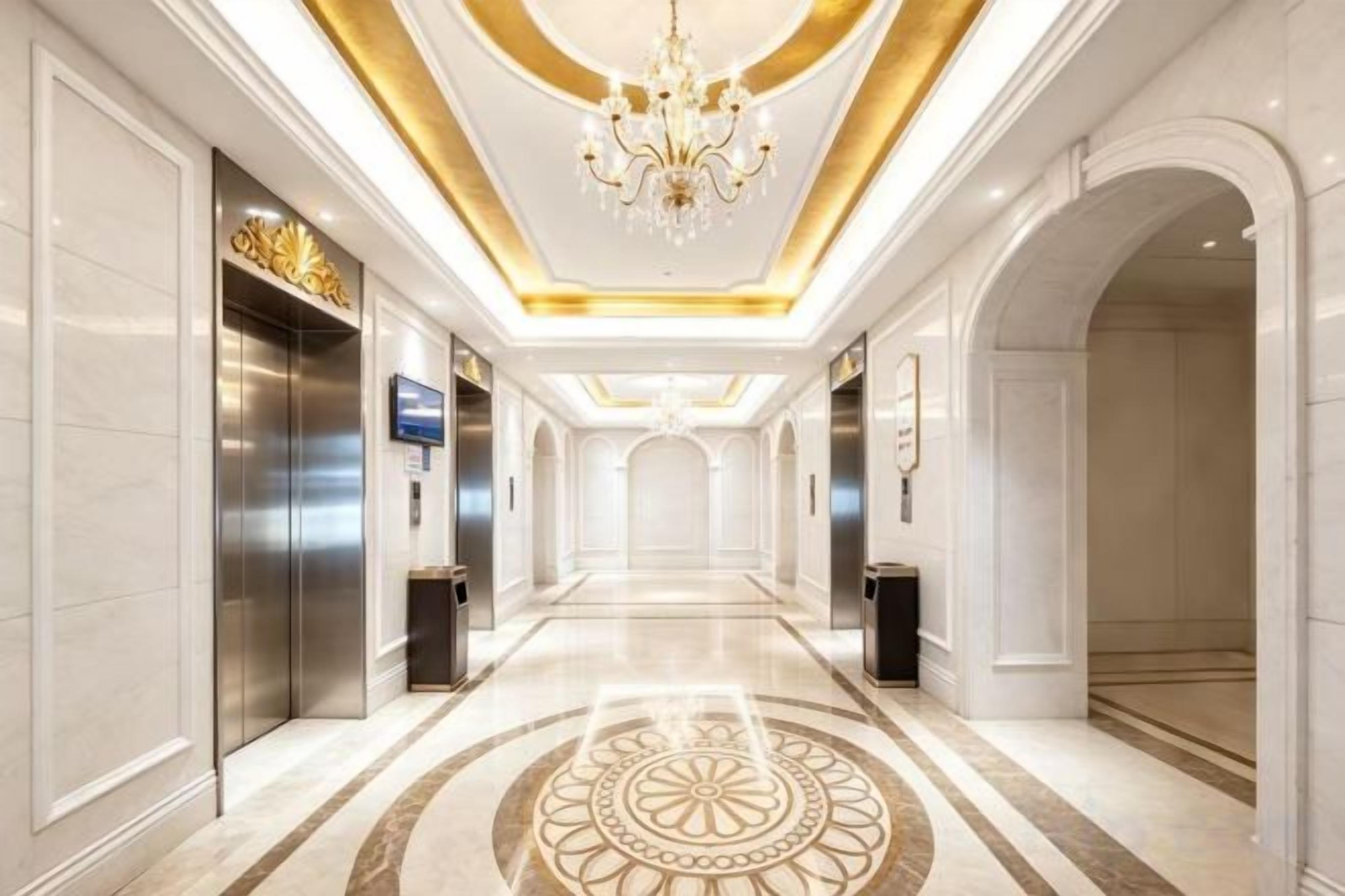 Un pasillo de hotel con candelabro, ascensores y suelo estampado.