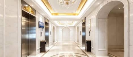 Un pasillo de hotel con candelabro, ascensores y suelo estampado.