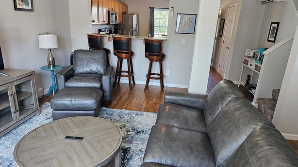 A living room with a leather sofa, a coffee table, and a bar area with stools. - Acadia Villas!  5B Hunter's Way:  A private neighborhood nestled in the woods. (Trenton)
