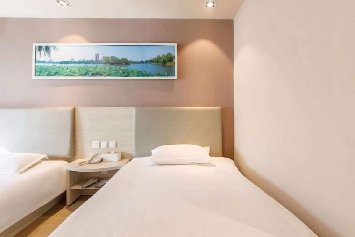 A hotel room with two beds, a nightstand with a phone, and a painting of a landscape on the wall.