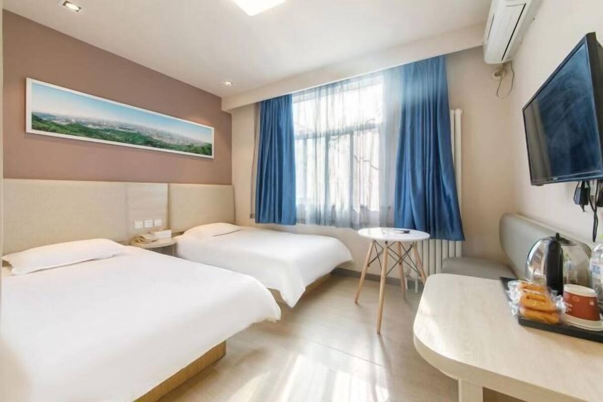 A hotel room with two beds, a small table, a television, and a window with curtains.
