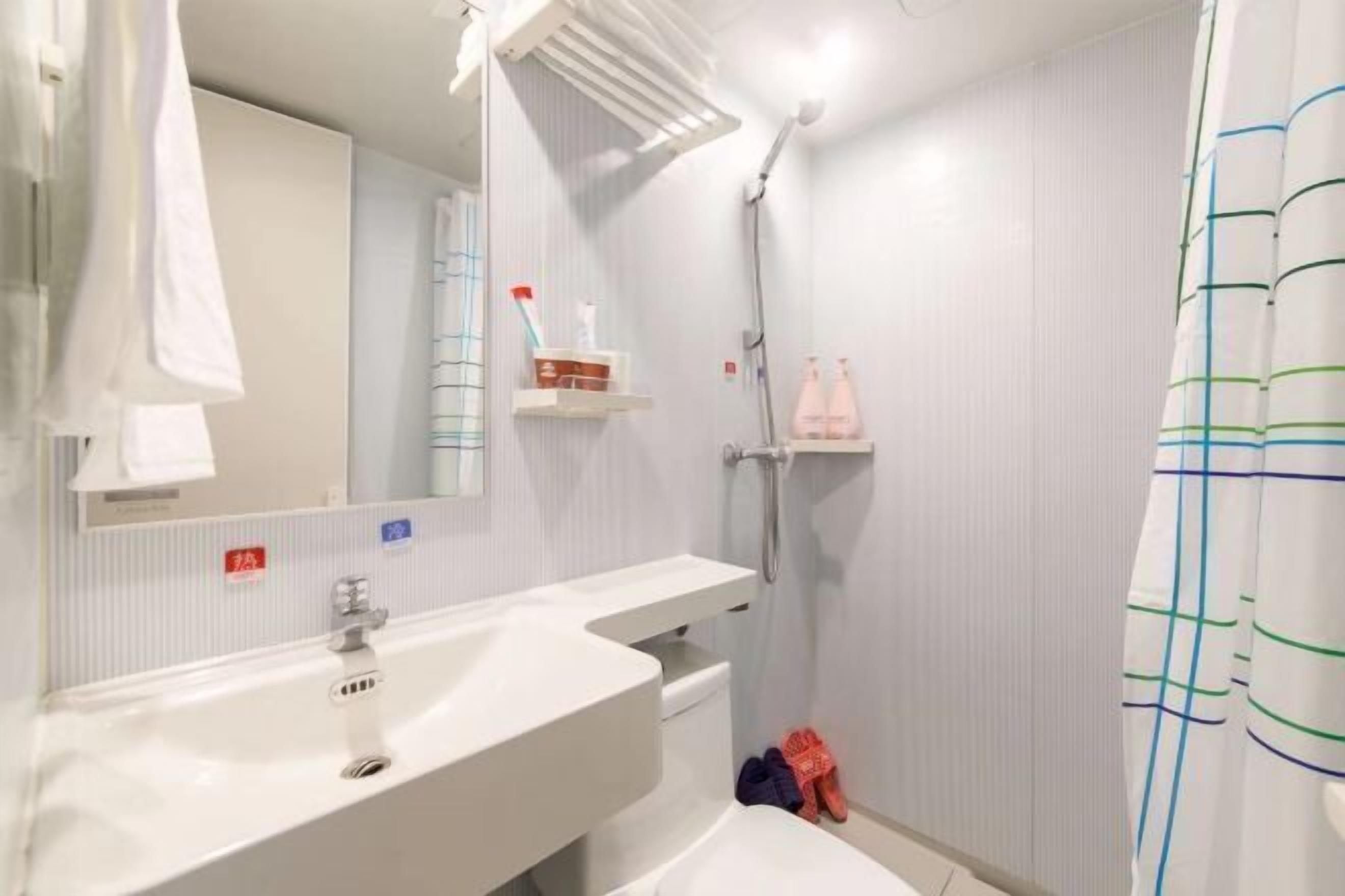 Un baño con lavamanos, espejo, ducha y toallero.