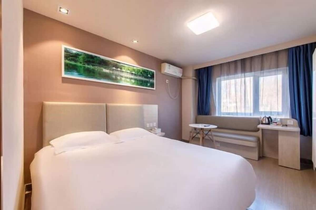 A hotel room with a large bed, a small table, a sofa, a painting on the wall, and a window with curtains.
