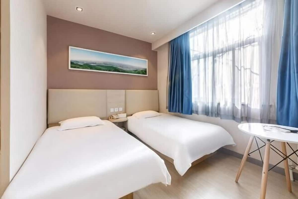 A hotel room with two beds, a bedside table, a desk, and a window with curtains.