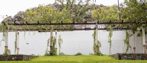 Una pérgola con luces de cuerda, un césped y un muro de piedra.