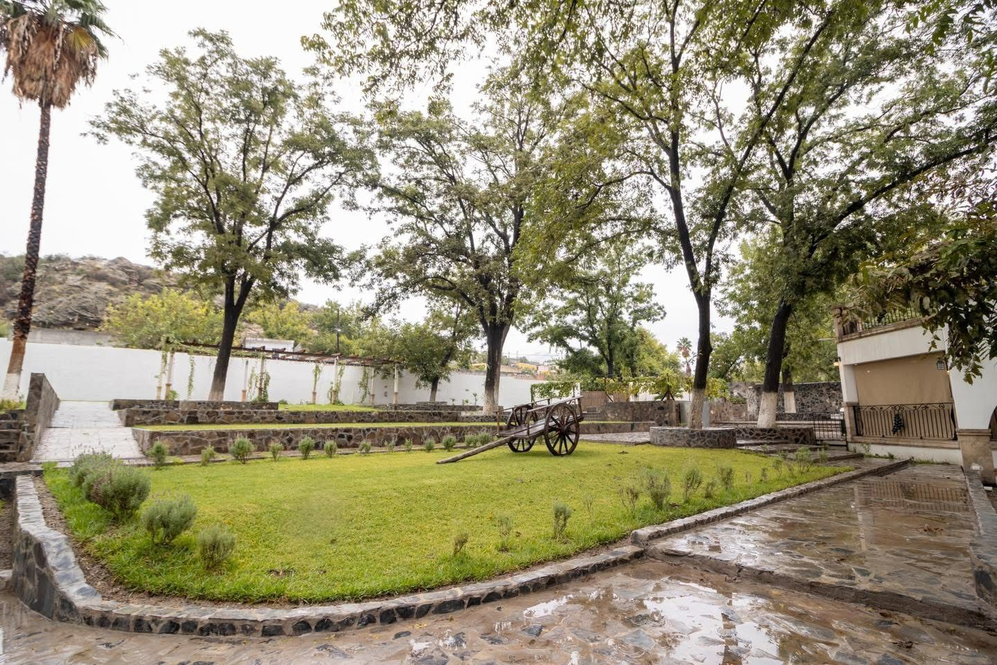 A courtyard with a grassy area, a stone pathway, and a wooden cart.