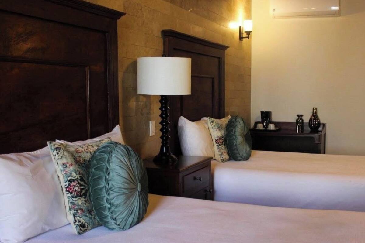 Une chambre d’hôtel avec deux lits, une table de chevet avec une lampe, un climatiseur fixé au mur et une petite table avec un vase et une tasse.