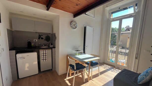 Una cocina funcional con refrigerador, pileta y alacenas. Hay una mesa de comedor con sillas y un reloj en la pared.