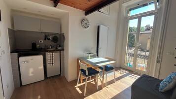 Una cucina compatta con frigorifero, lavello e pensili. Si vede un tavolo con sedie e un orologio appeso al muro.