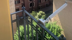 Vista desde un balcón con vista a un edificio con múltiples ventanas y un árbol en primer plano.