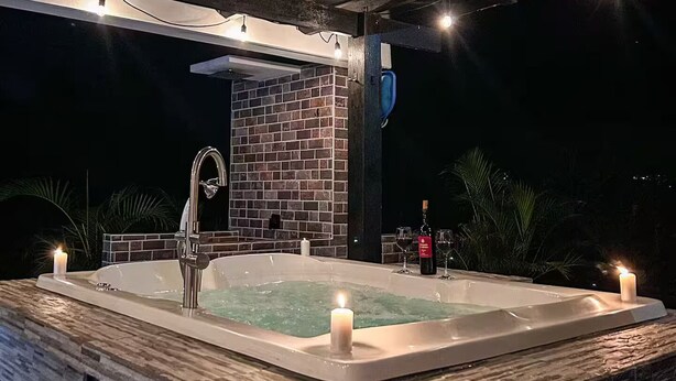 An outdoor hot tub with a stone wall backdrop, a faucet, and candles.