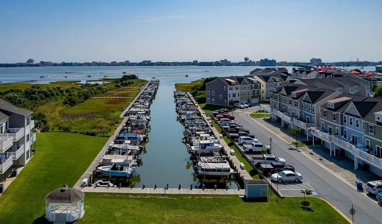 A marina with boats docked in a long, narrow waterway, surrounded by residential buildings with balconies and a gazebo.
