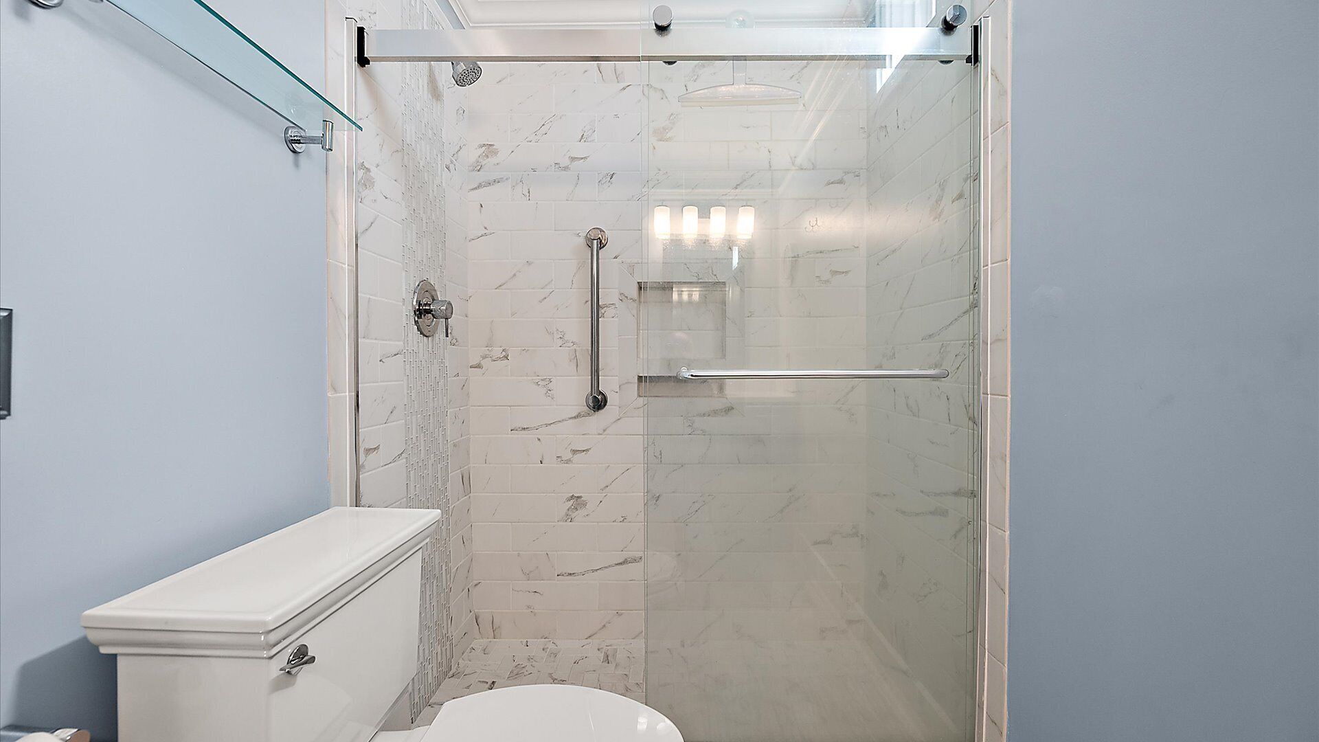 A modern bathroom with a glass-enclosed shower, white marble tiles, and a toilet.