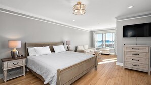 Un dormitorio moderno con una cama grande, mesitas de noche, televisión y vistas a la ciudad.