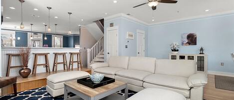 A modern living room with a white sofa, a coffee table, and a kitchen area with bar stools.