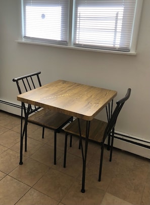 Una mesa de comedor con cuatro sillas, una ventana con persianas y un piso de baldosas.