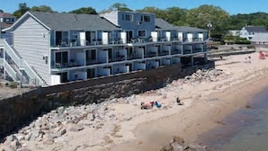 Un hôtel à plusieurs étages doté de balcons, situé près d’une plage où l’on peut voir des travaux de construction en cours et des débris.
