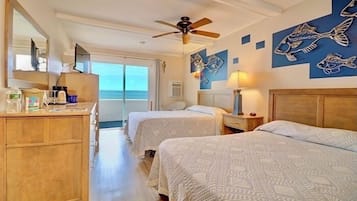 A hotel room with two beds, a wooden dresser, a ceiling fan, and artwork of fish on the walls.