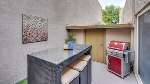 A patio with a glass-top table, cushioned seating, a grill, and a painting on the wall. - 3BR/2 Bath w/Pool & Hot Tub- Scottsdale Entertainment District (Scottsdale)