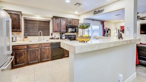 A modern kitchen with dark wooden cabinets, a central island, stainless steel appliances, and a bright ceiling. - 3BR/2 Bath w/Pool & Hot Tub- Scottsdale Entertainment District (Scottsdale)