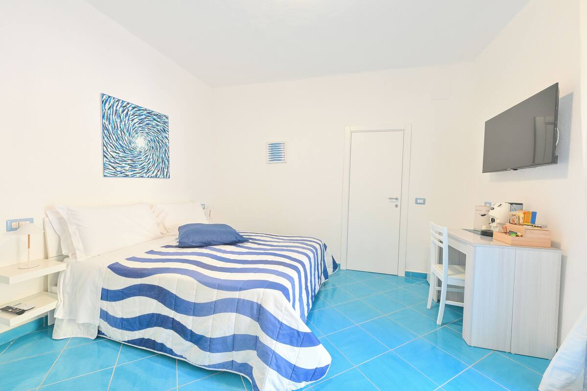 A bedroom with a bed, a desk, a chair, a TV, and a wall art piece.