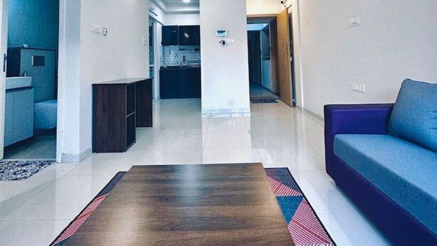 Una sala moderna con una mesa de centro de madera, un sofá azul y una cocina al fondo.