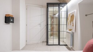 Una stanza con una porta bianca, una porta scorrevole in vetro che dà su un bagno e un termosifone sulla parete.
