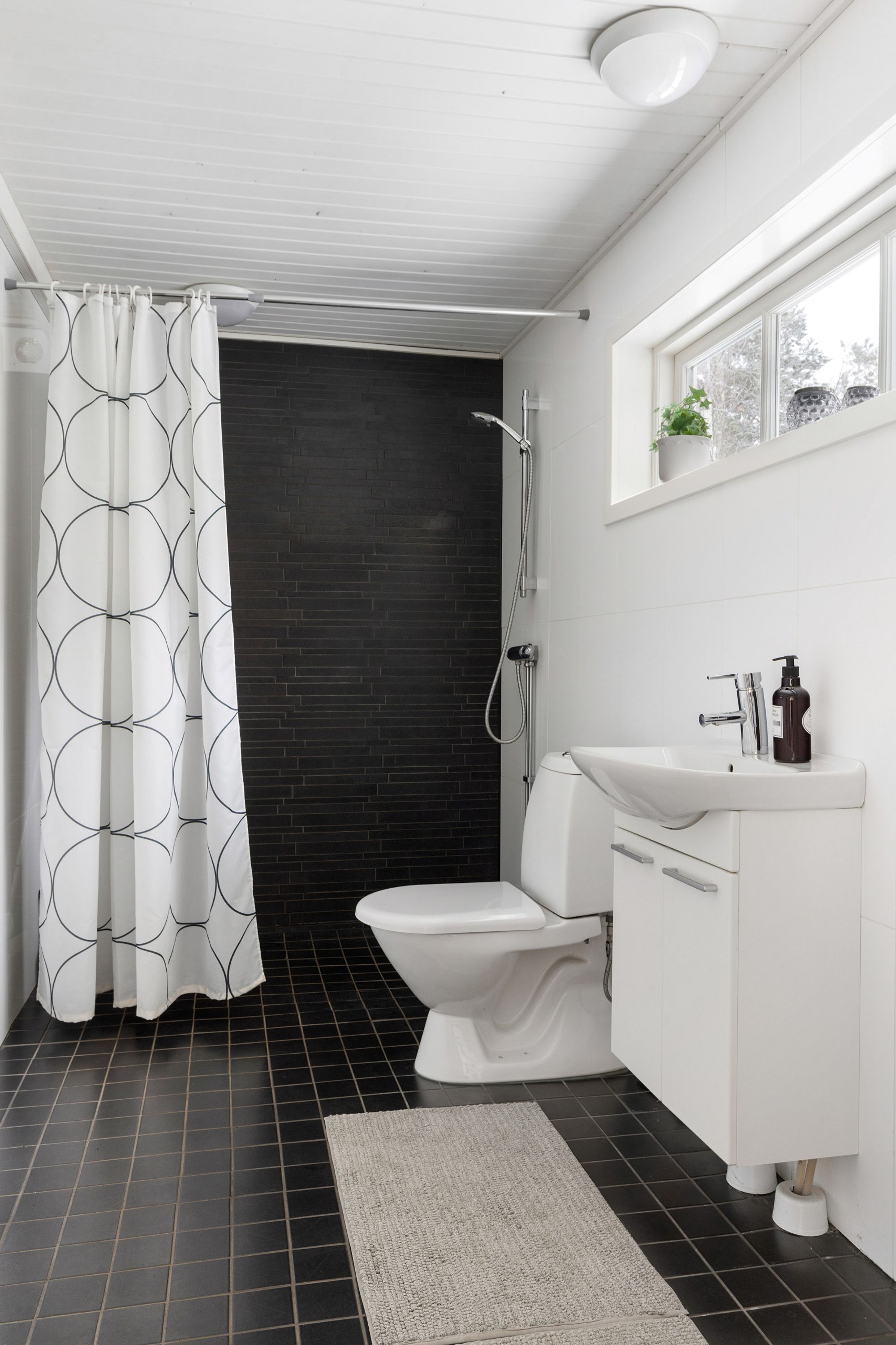 A modern bathroom with a white toilet, dark tiled floor, and a shower area.