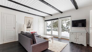 A modern living room with a gray sofa, white walls, a wooden ceiling, a television, and a view of the outdoors. - Dream Cottage in the Stockholm Archipelago (Djurhamn)