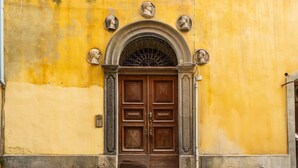 A yellow building with a wooden double door, a stone archway, and three busts above the door.