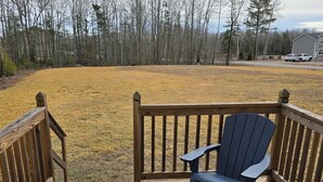 En træterrasse med en blå Adirondack-stol og en bænk, med udsigt over en græsplæne og et skovområde.