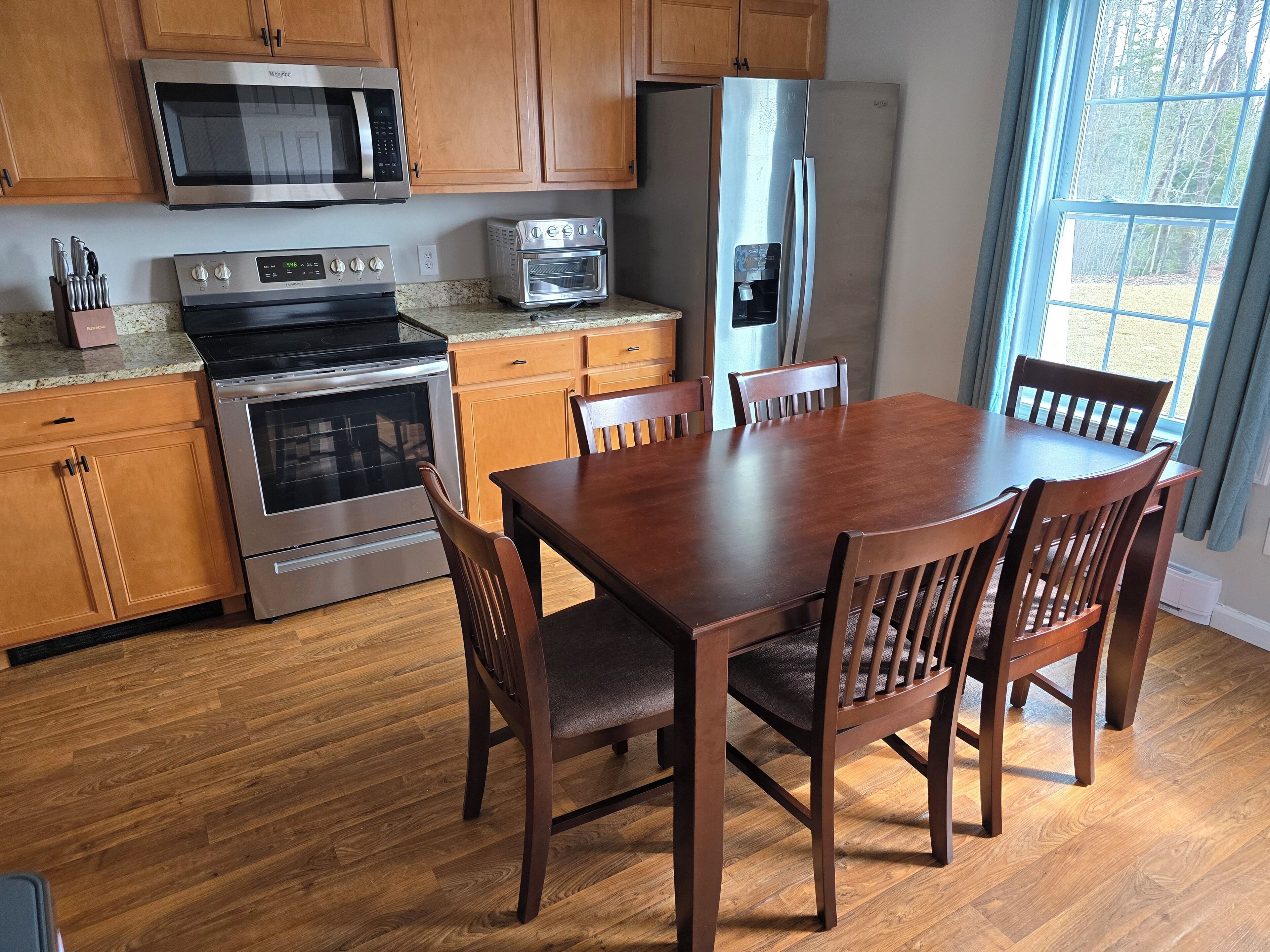 A kitchen with wooden cabinets, a microwave, an oven, a toaster, and a refrigerator.