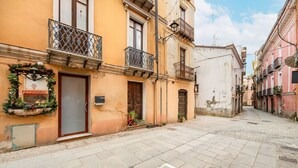 A narrow street with buildings featuring balconies and a shop with a sign. - Guest Room Historic Centre (Iglesias)